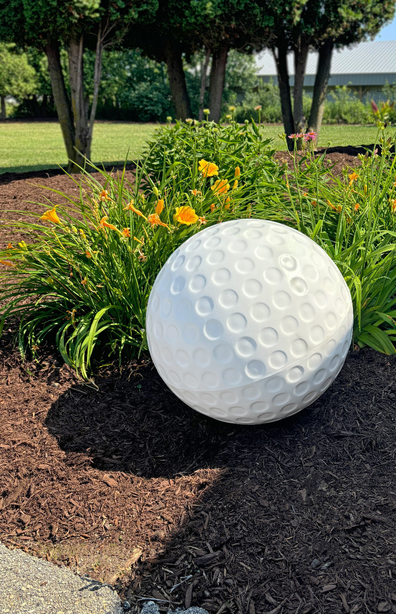 Giant Plastic Golf Ball Displayed Outdoors in a Garden Bed 